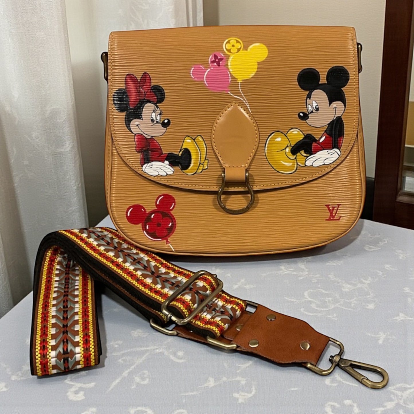 Designer handbag with cartoon characters and colorful strap on a light surface.