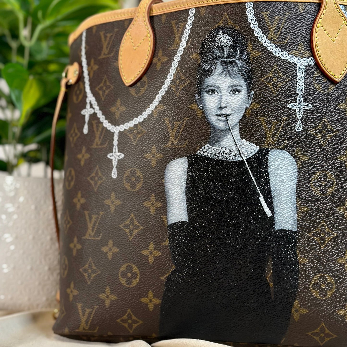 Designer Louis Vuitton handbag with a monogram pattern and a hand painted design of Audrey Hepburn in a black dress.