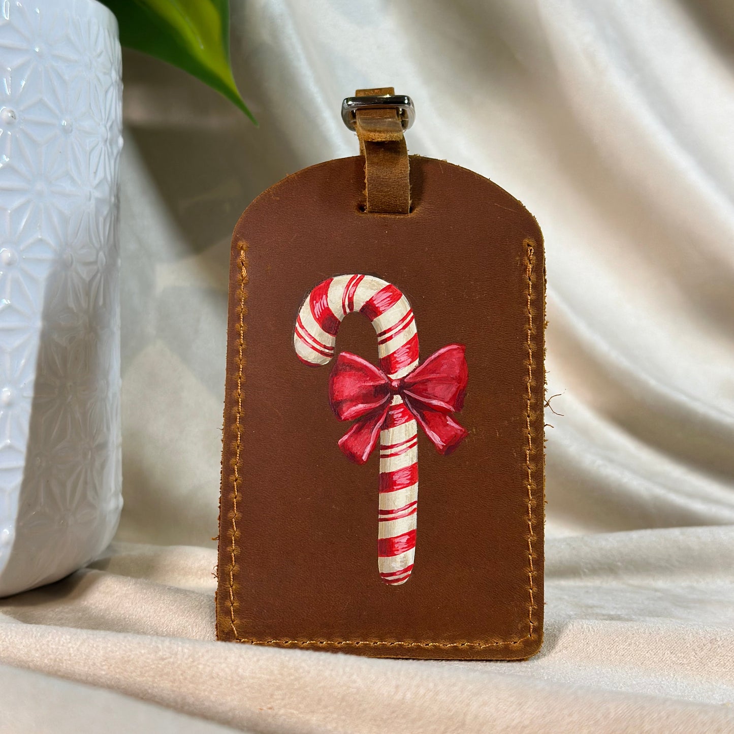 Brown leather luggage tag with candy cane and bow design on a white surface.