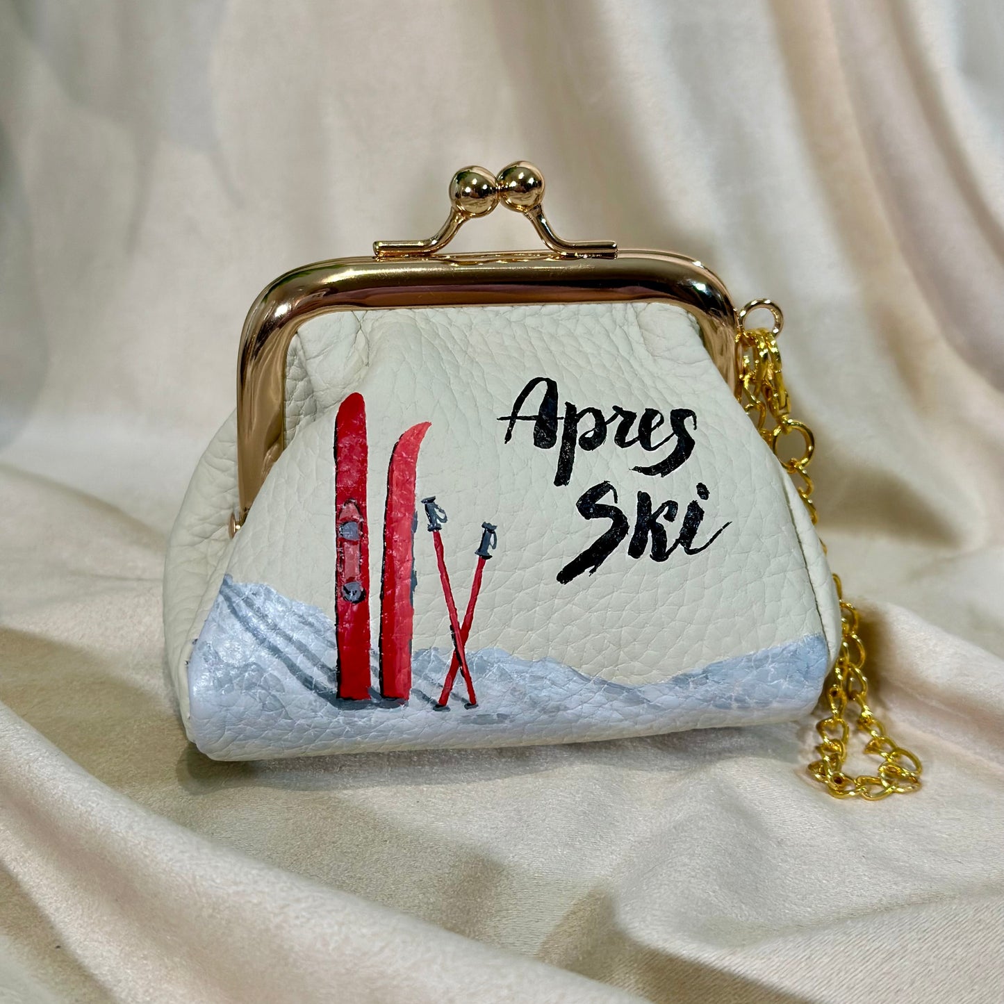 Small handbag with skis and 'Apres Ski' text on a beige fabric background