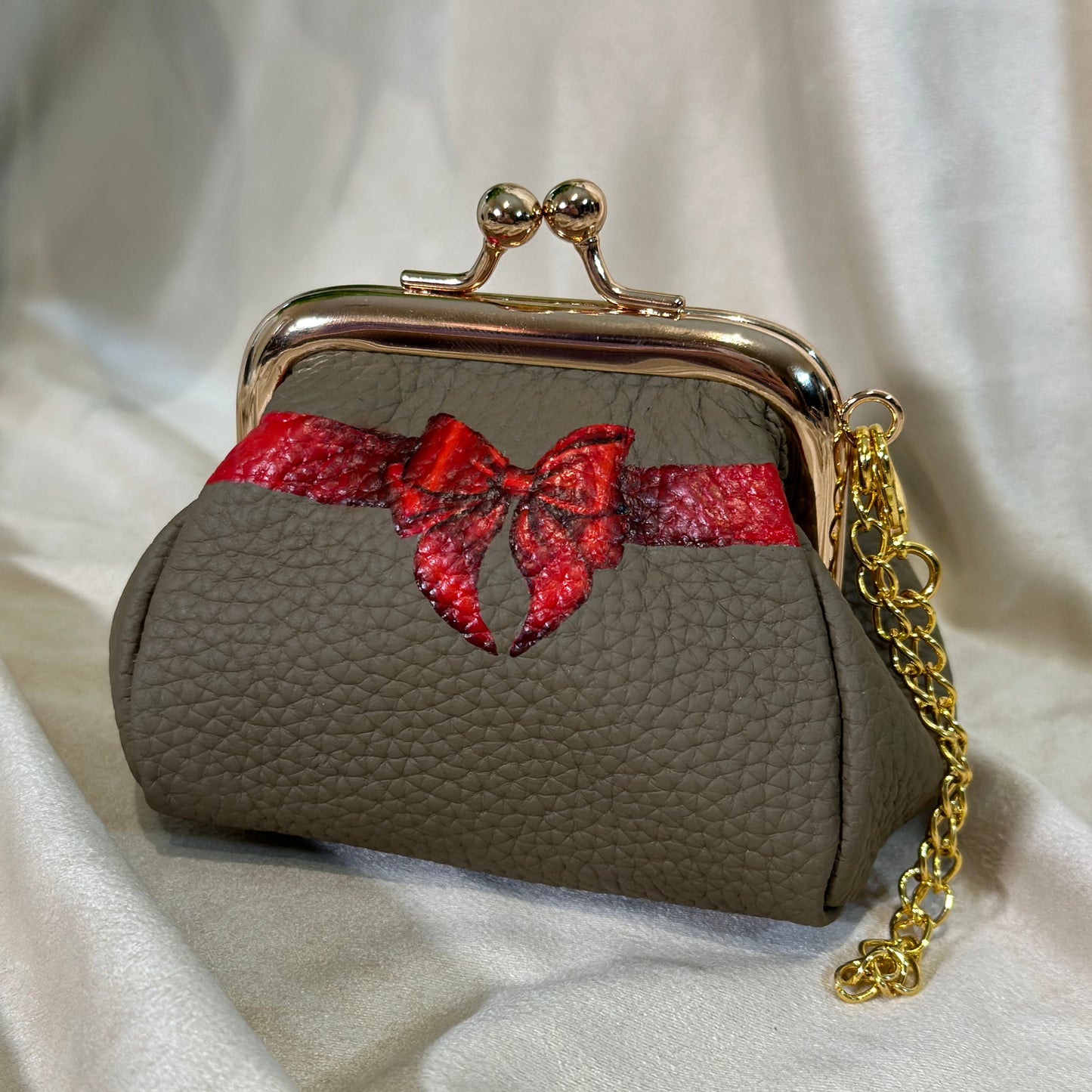 Small brown purse with a red bow on a white fabric background