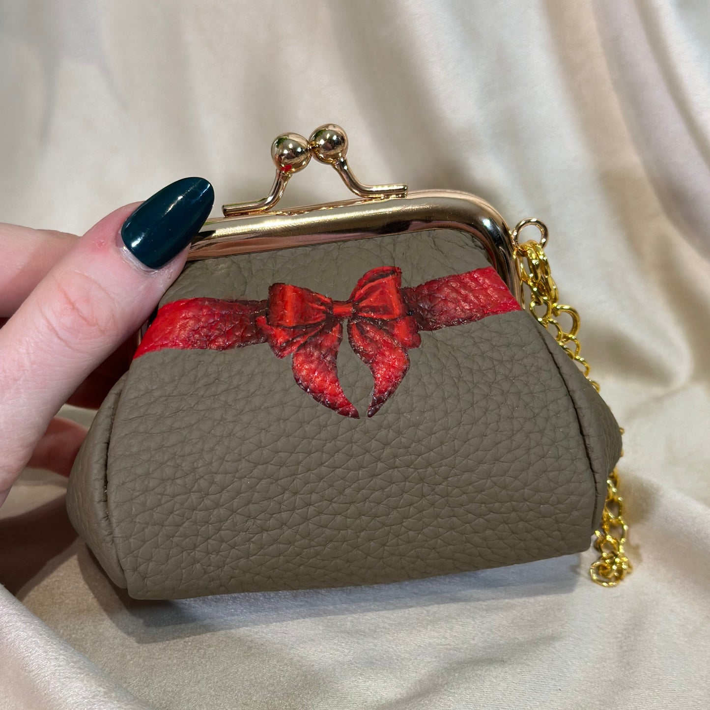 Small beige handbag with a red bow detail held by a hand against a beige background