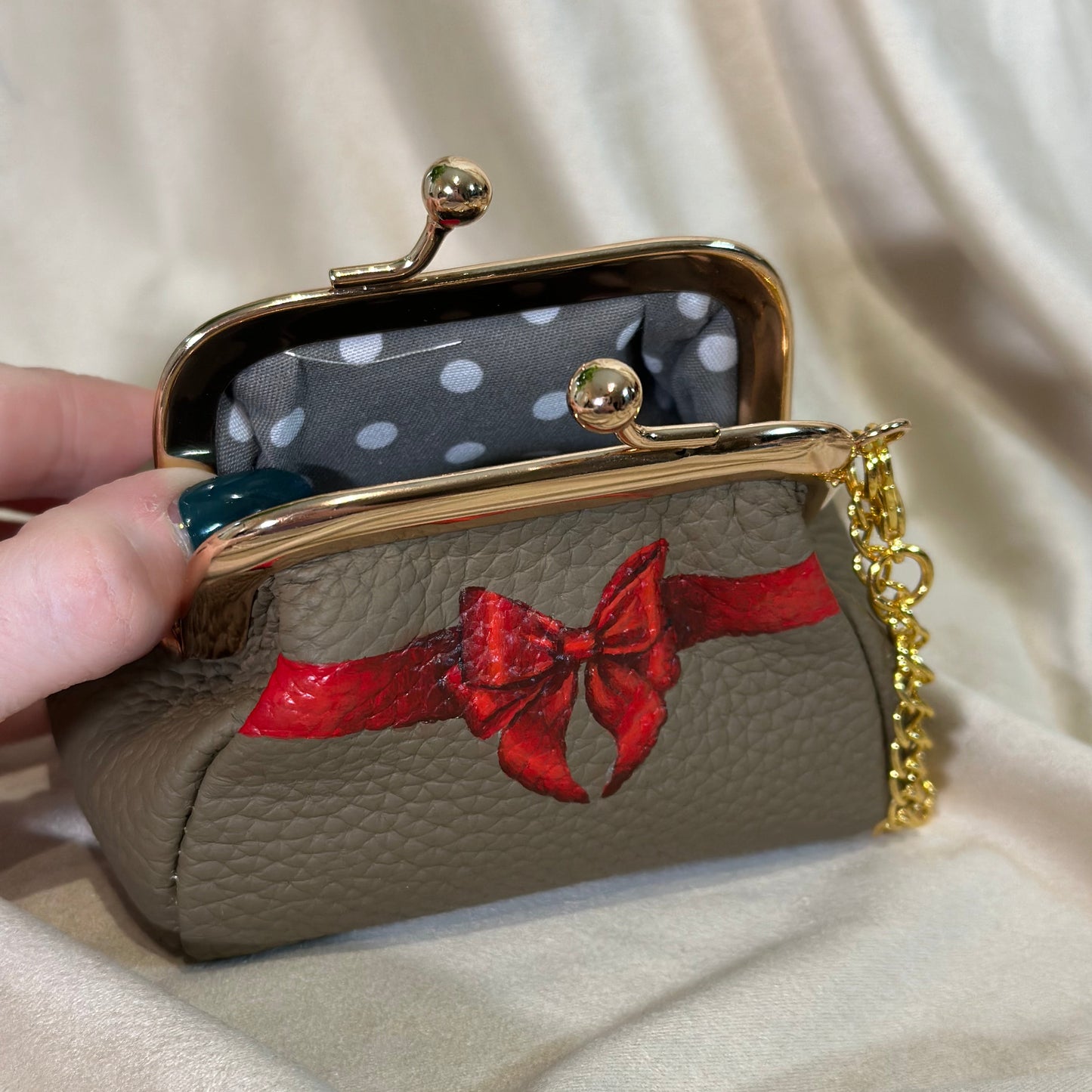 Handbag with red bow design held by a hand against a beige fabric background