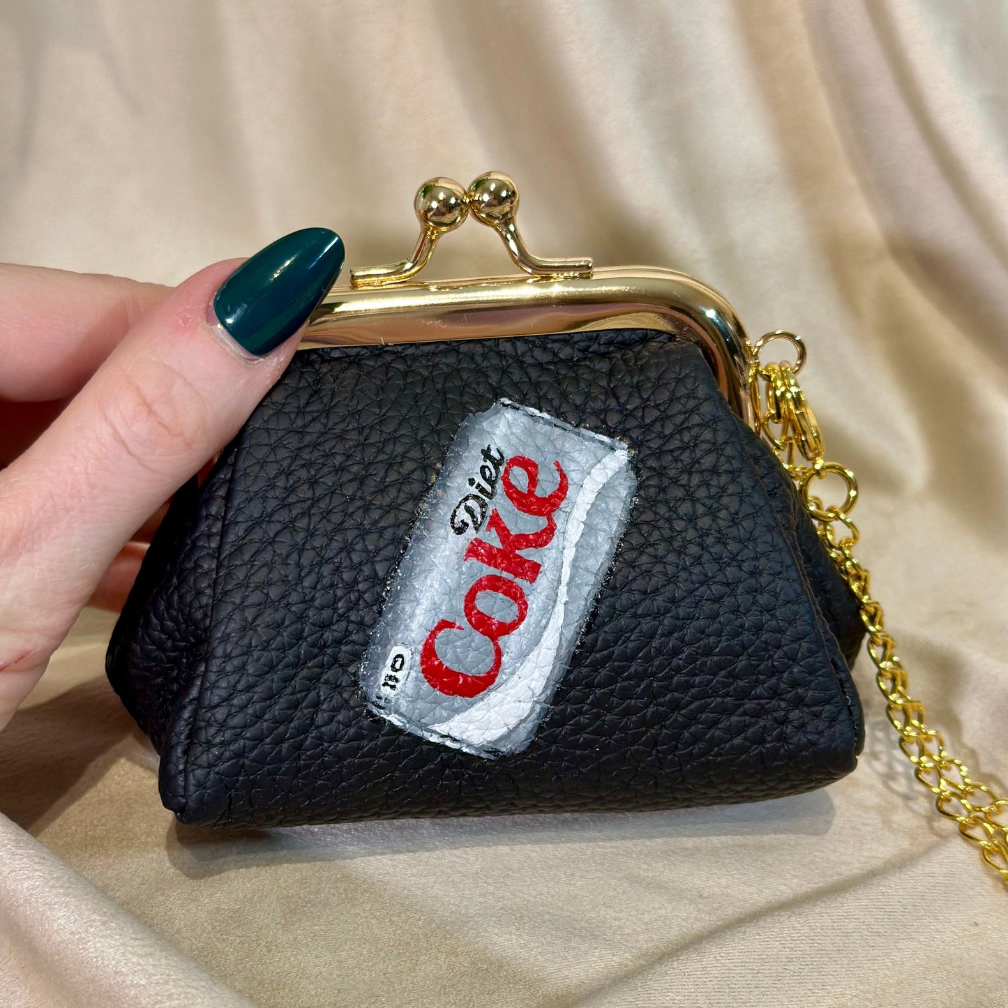 Black pouch with a Coca-Cola patch held by a hand on a beige fabric background