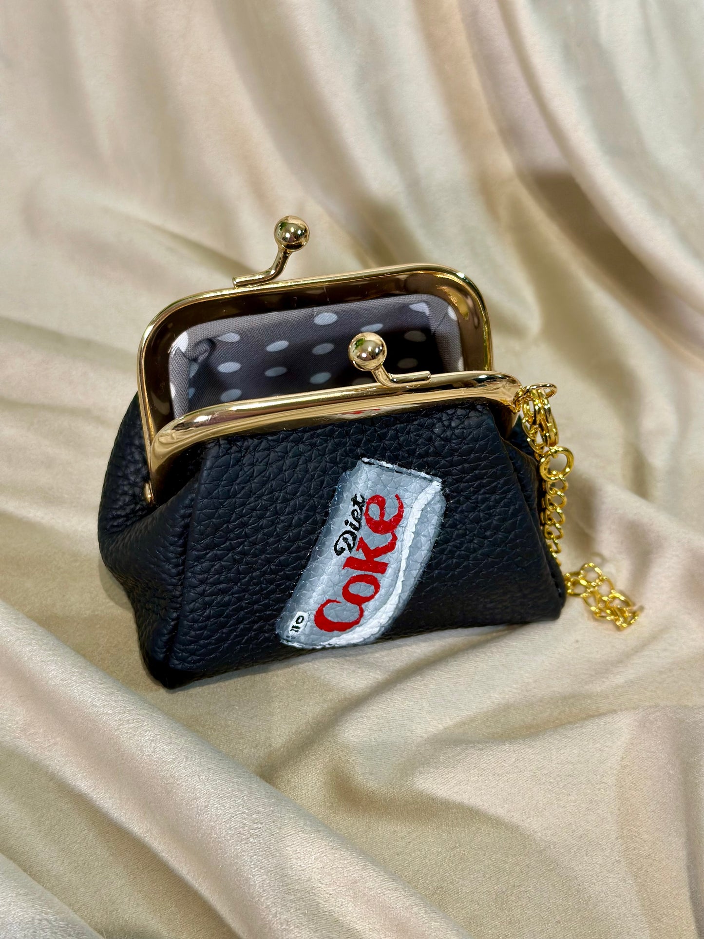Black handbag with gold clasp and 'Coca-Cola' logo on a beige fabric background