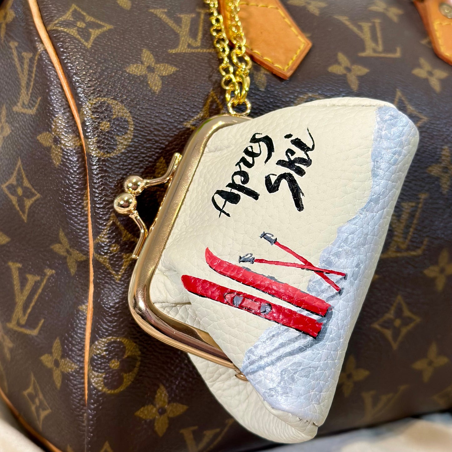 Small pouch with skiing design in front of a Louis Vuitton bag