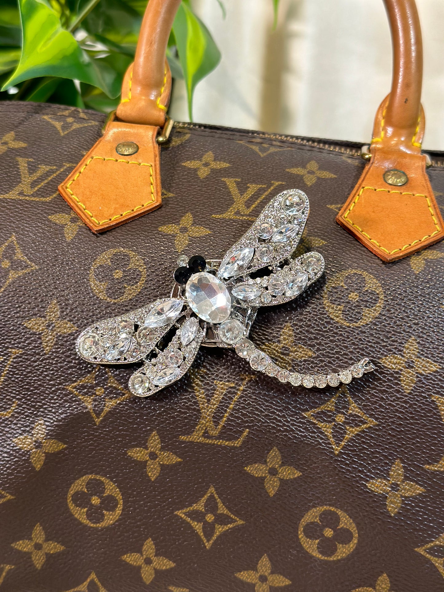 Silver bee-shaped brooch on a Louis Vuitton handbag with monogram pattern.