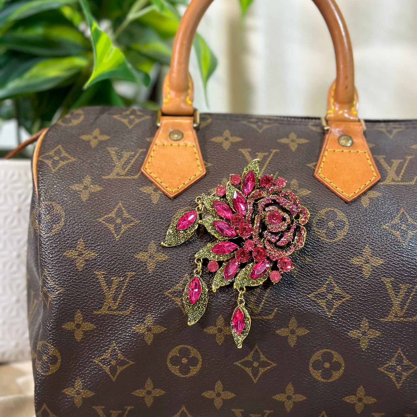 Designer handbag with a decorative brooch featuring pink gemstones.