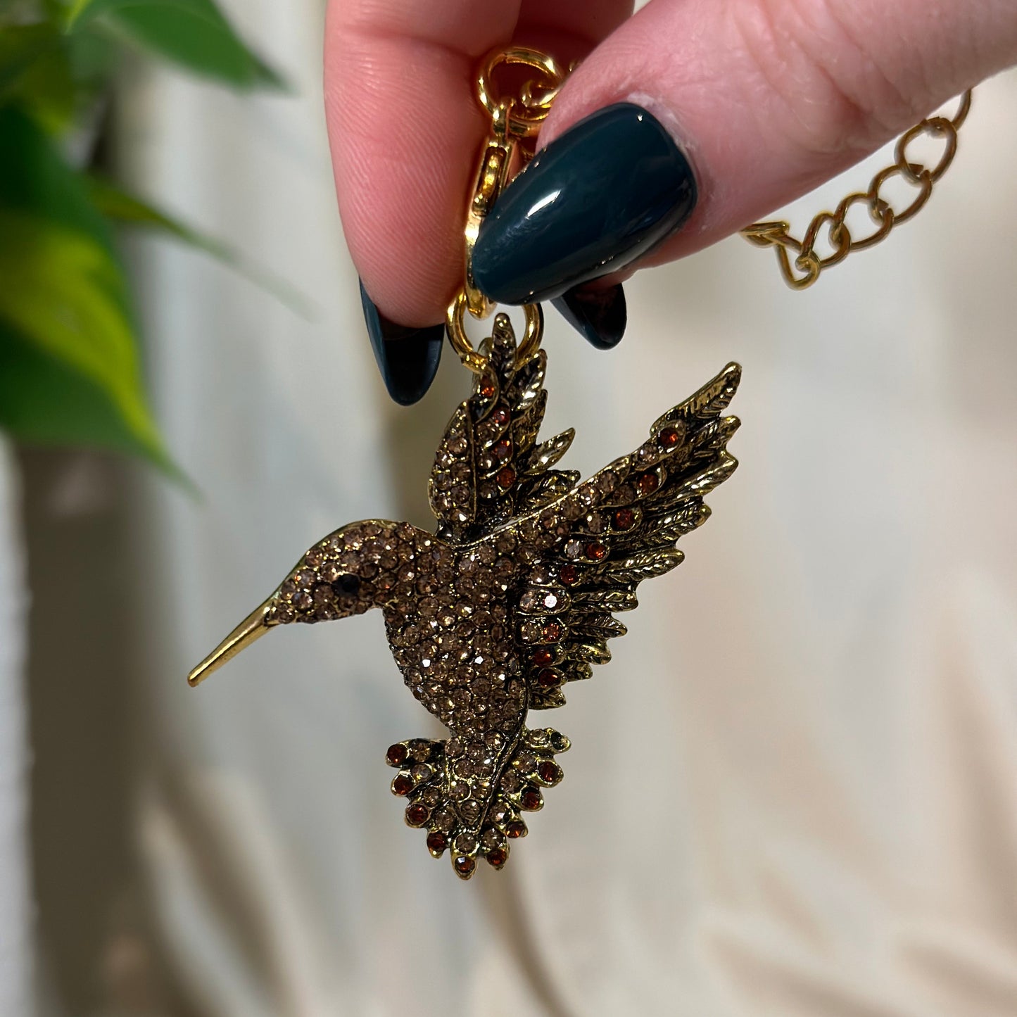 Hand holding a gold necklace with a detailed leaf pendant against a neutral background