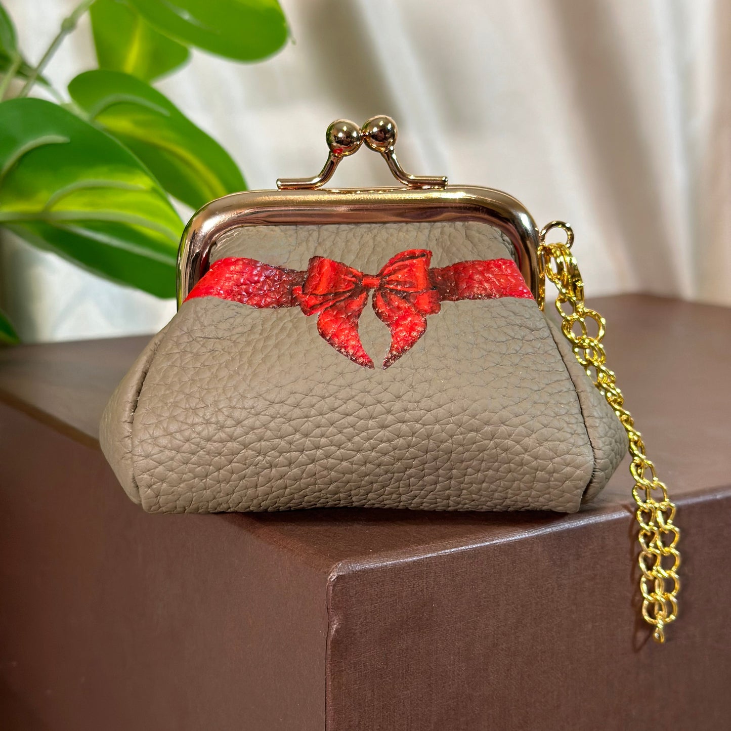 Beige handbag with red floral design and gold chain strap on a blurred background