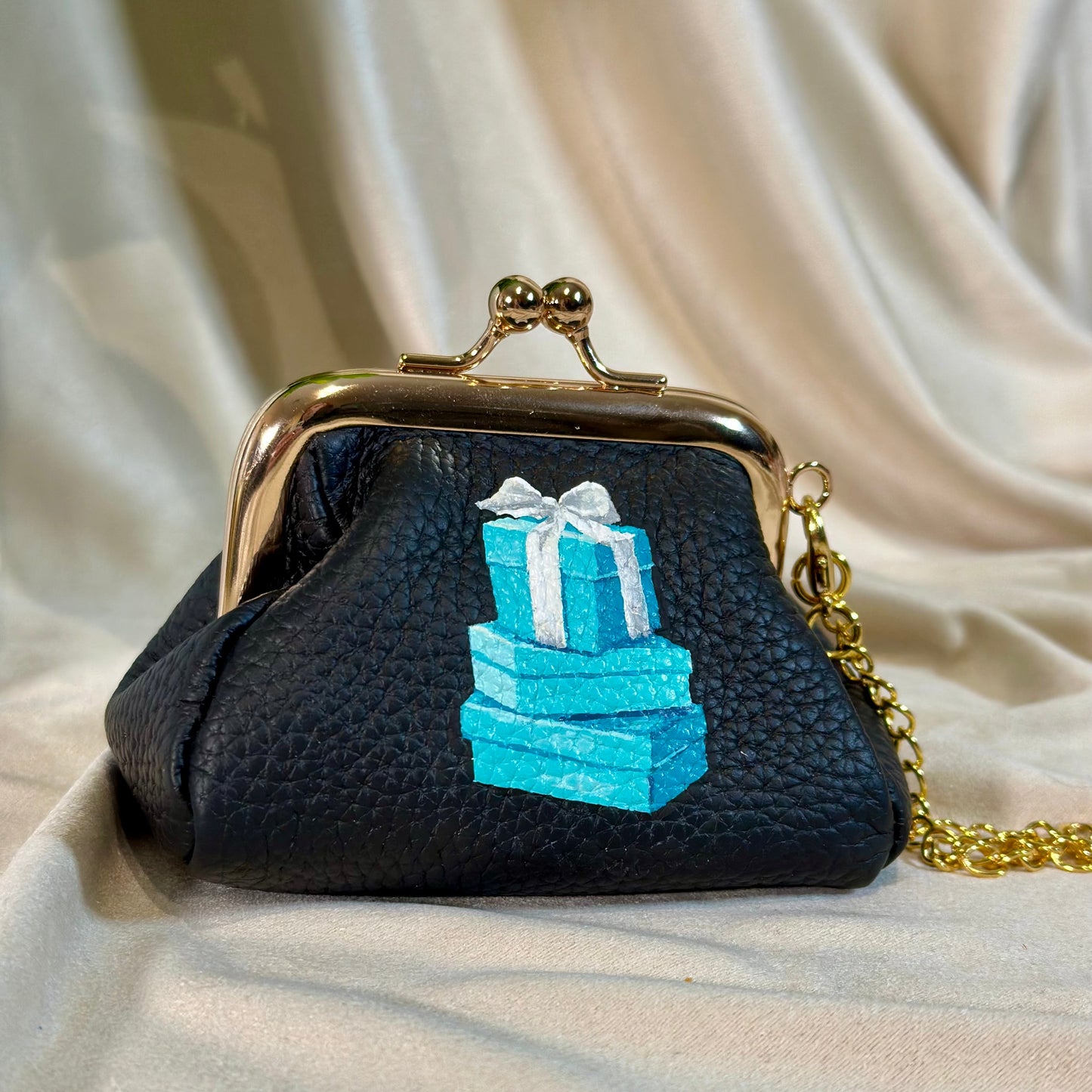 Black handbag with blue gift box design on a beige fabric background
