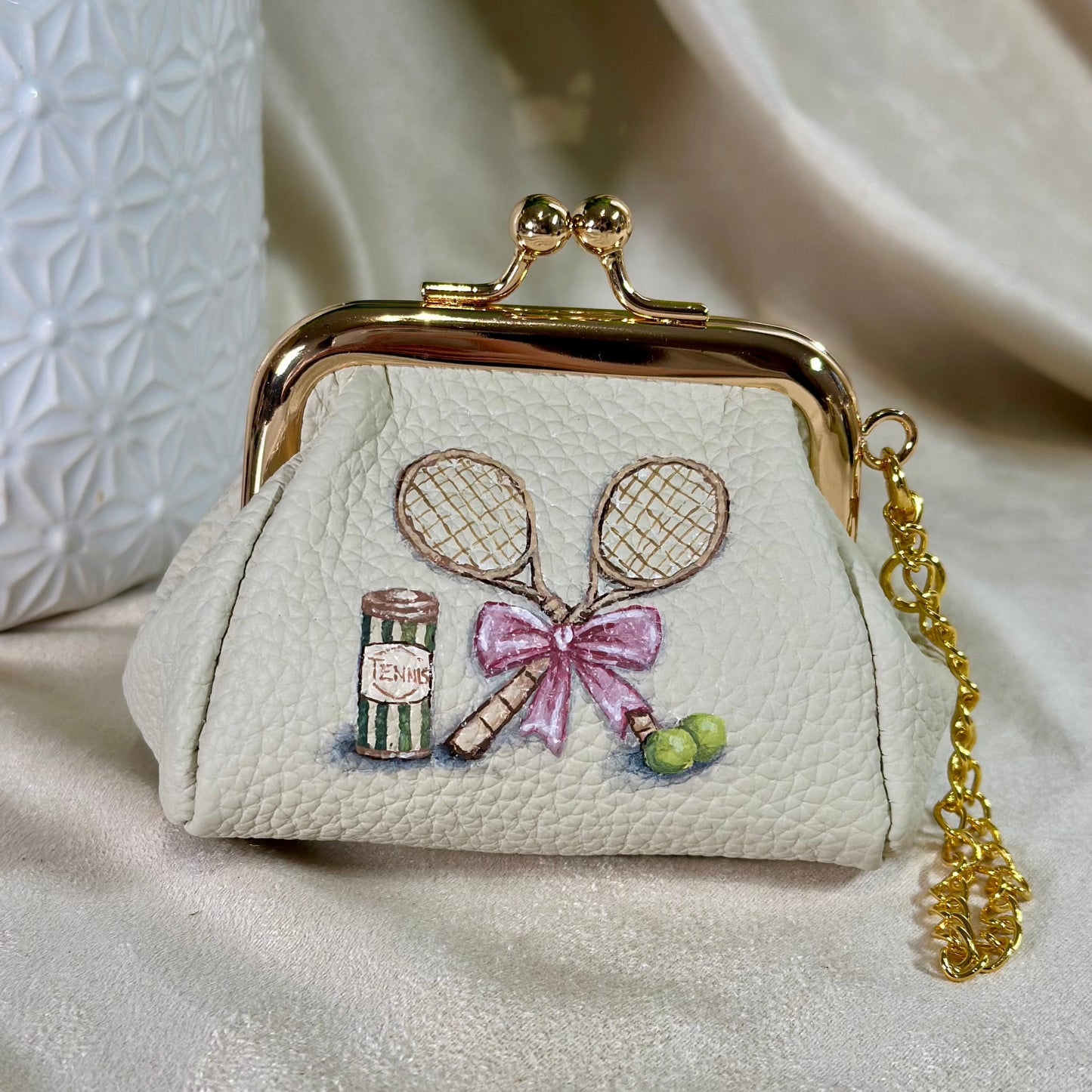 Small white purse with embroidered tennis racket, can, and ball design on a light background