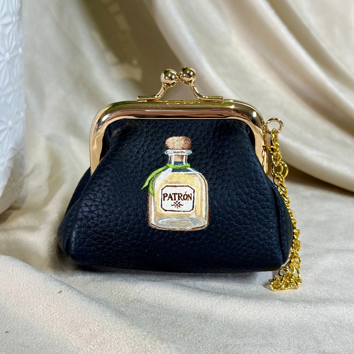 Black purse with Patron bottle design on a white fabric background