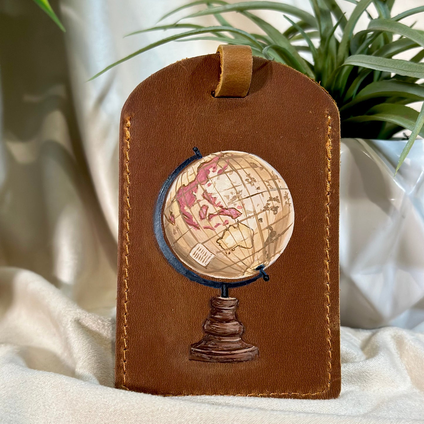 Brown leather luggage tag with globe design on a light fabric background