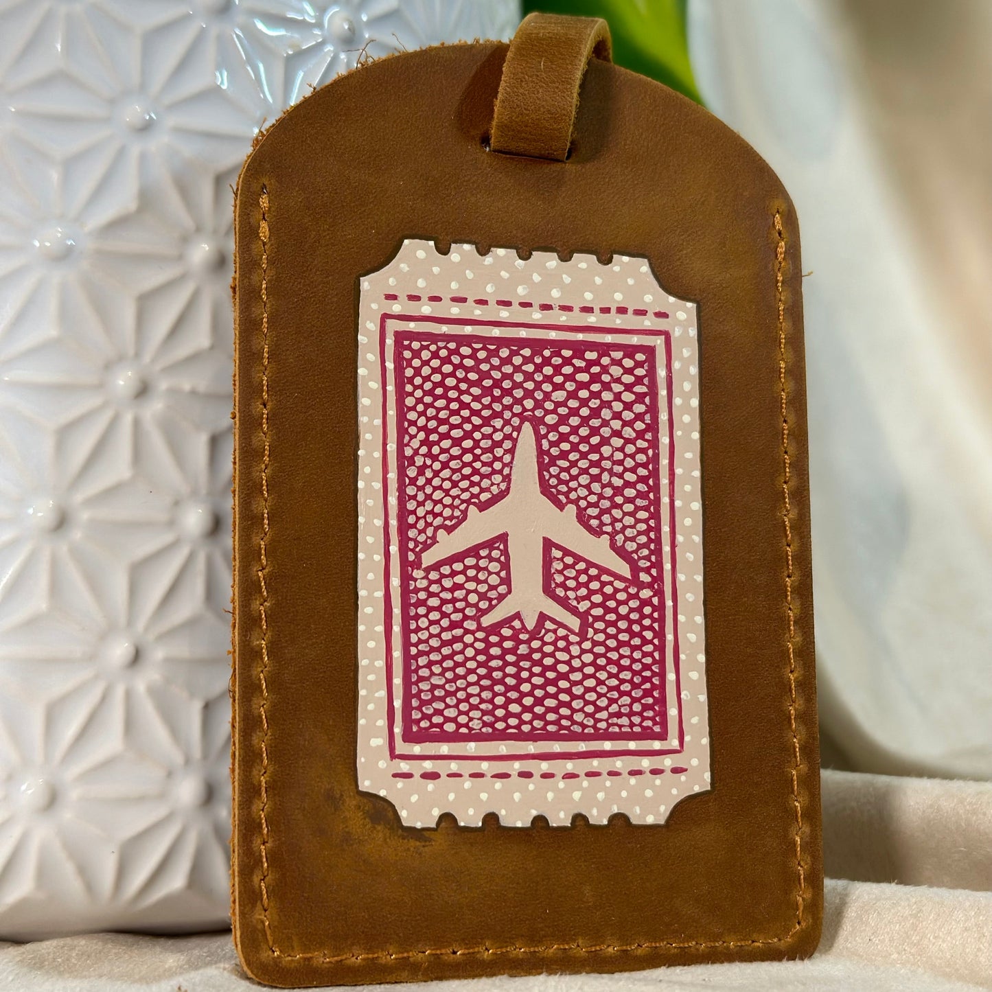 Brown leather luggage tag with airplane design on a textured surface