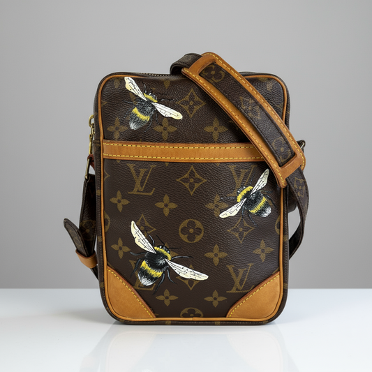 Designer bag with bee pattern next to a glass of paintbrushes on a marble surface.