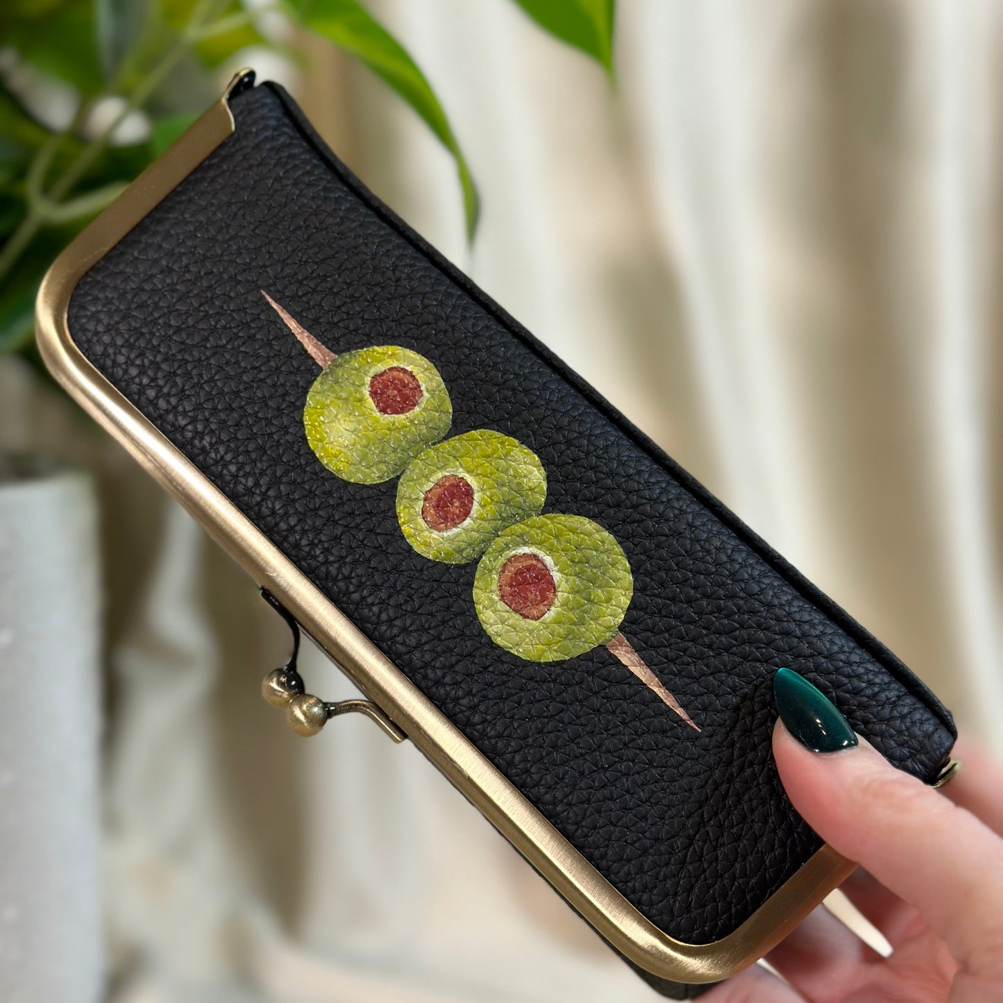 Black phone case with green olives design held by a hand