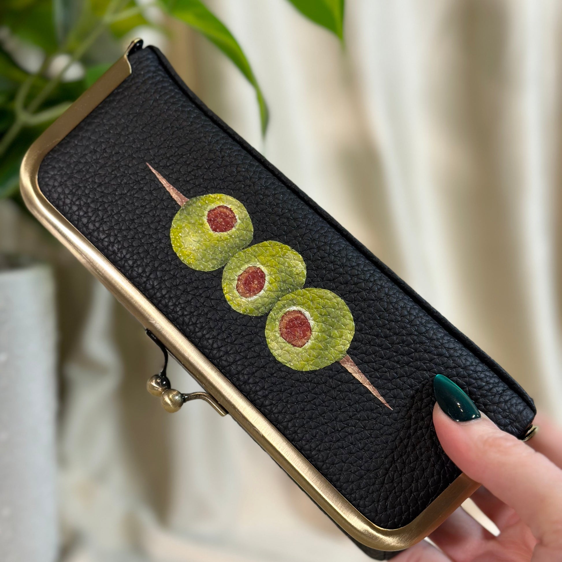 Black phone case with green olives design held by a hand
