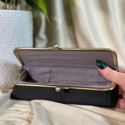 Black clutch with gold frame held by a hand against a neutral background