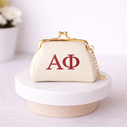 Small cream-colored purse with red letters 'AΦ' on a white surface