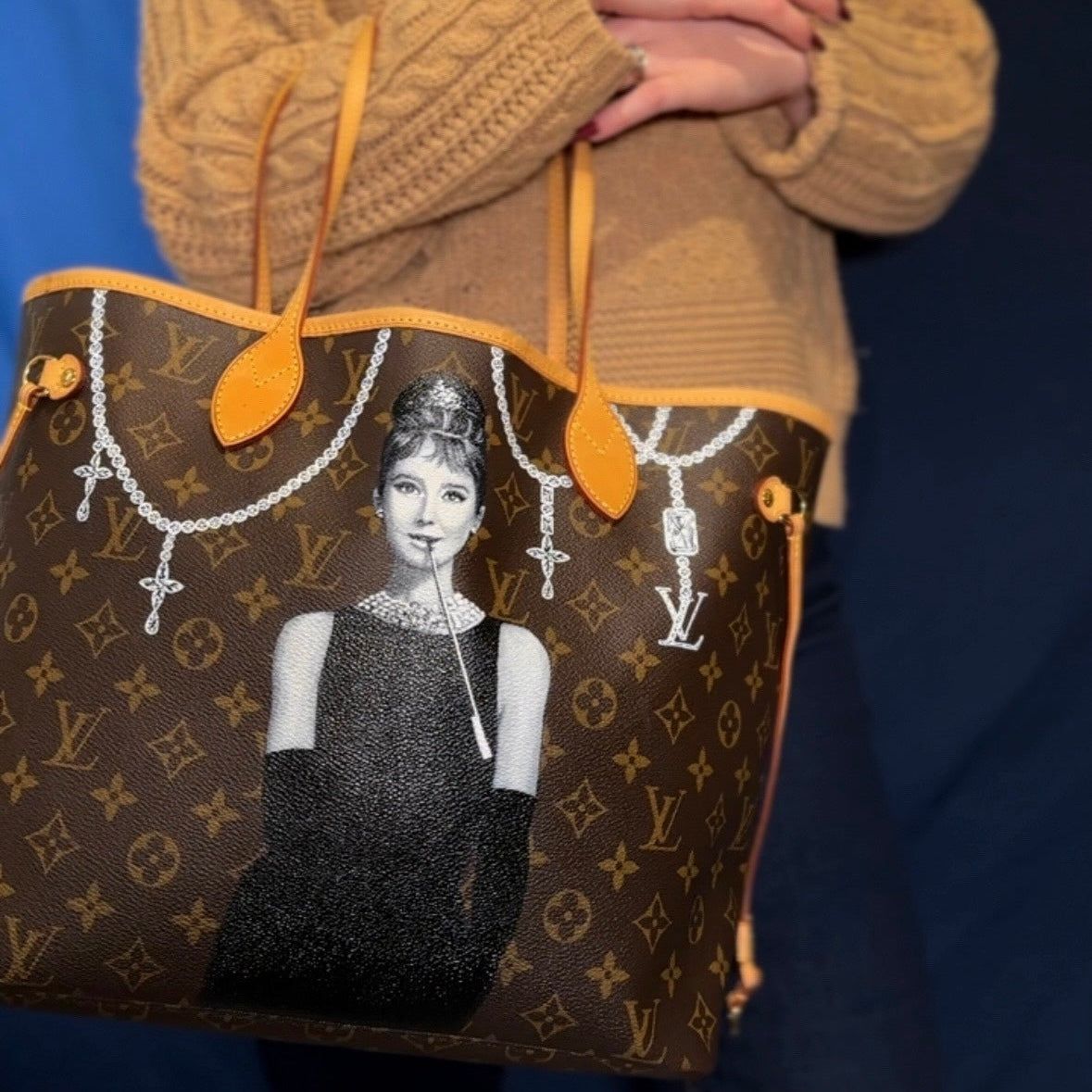 Person holding a brown handbag with a graphic design on a dark background