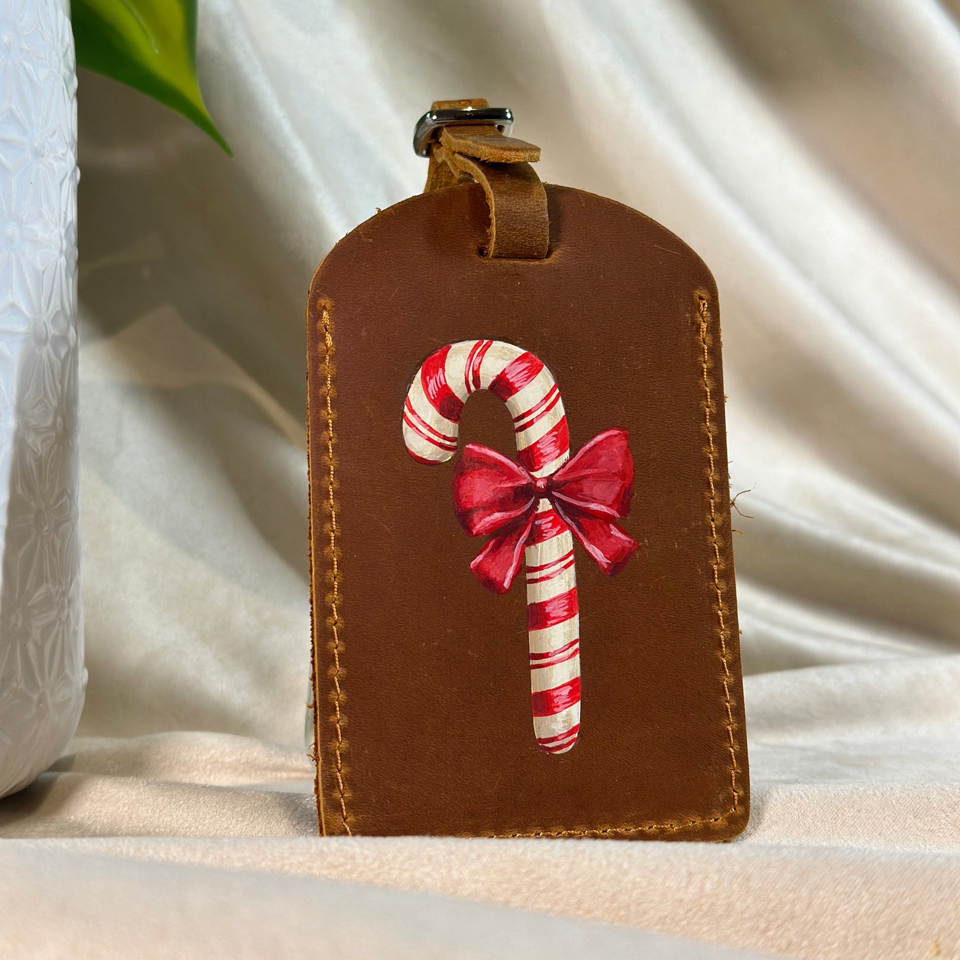 Brown leather luggage tag with candy cane and bow design on a white fabric background