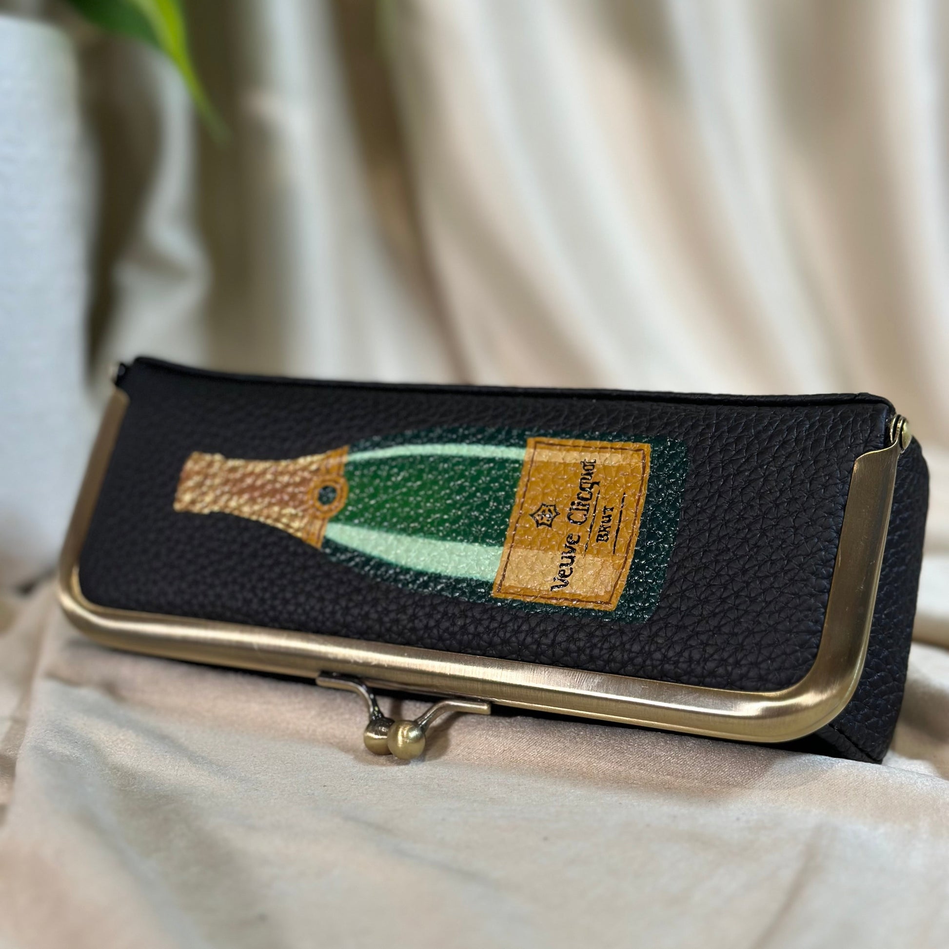Black clutch with champagne bottle design on a light fabric background