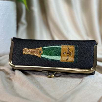Black pouch with champagne bottle design on a beige fabric background