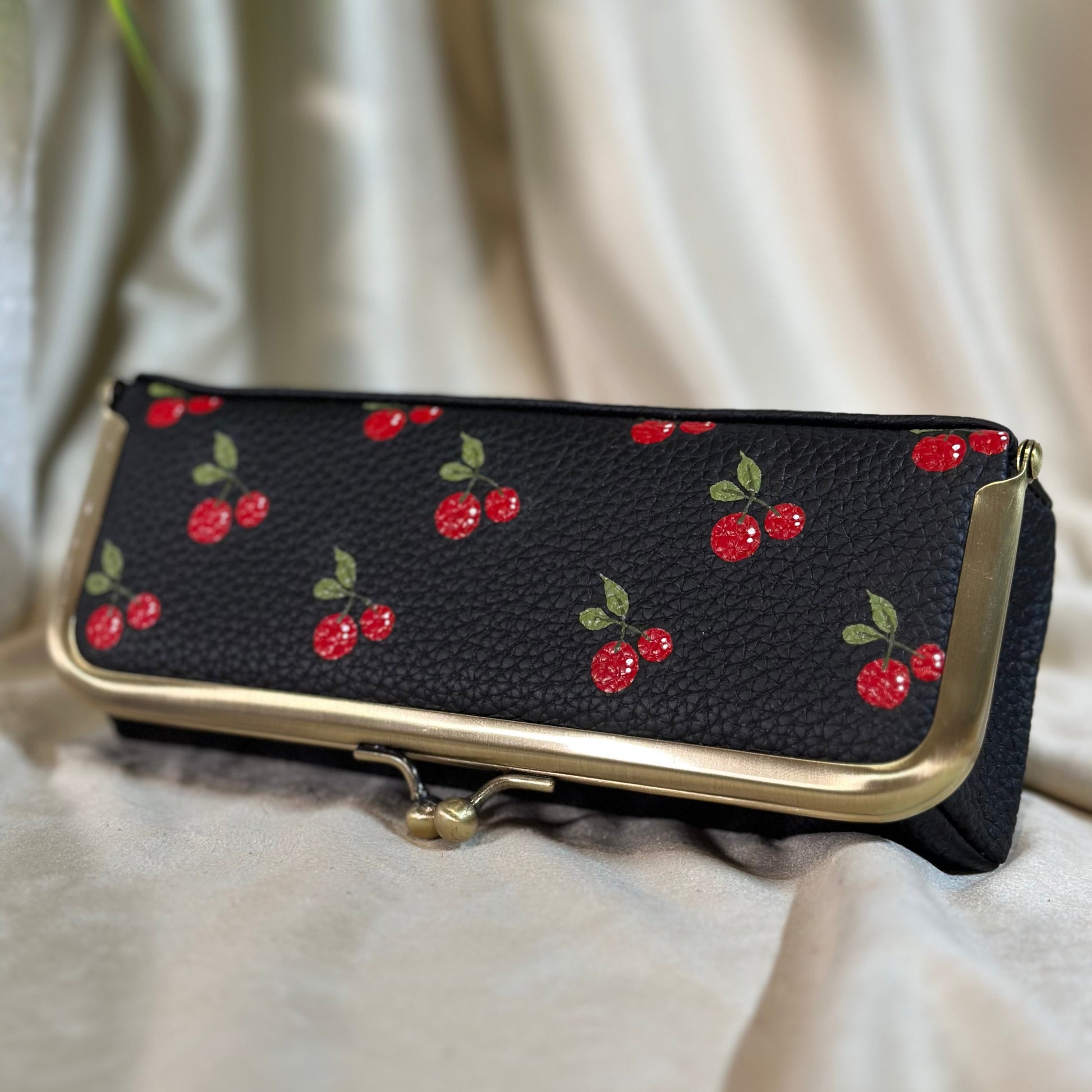 Black pouch with red cherry pattern on a white fabric background