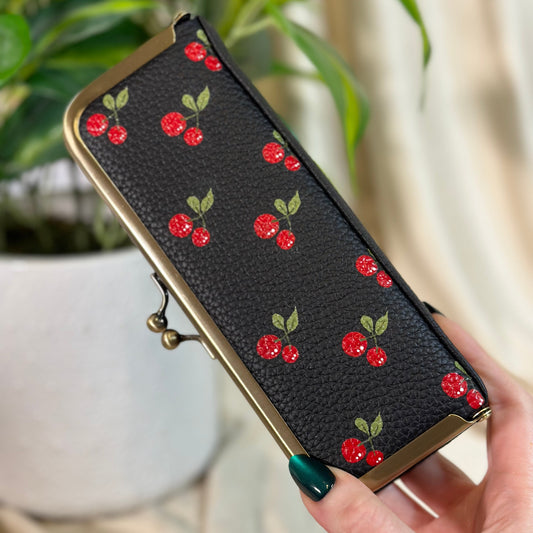 Black wallet with red cherry pattern held by a hand against a blurred indoor background