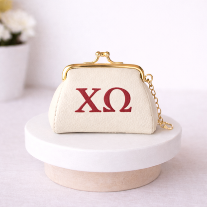 Small cream-colored purse with gold clasp and chain, featuring red 'ΧΩ' letters on a white surface.
