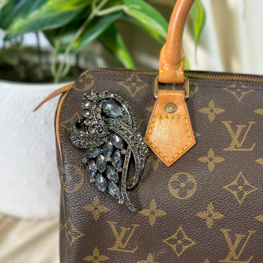 Louis Vuitton handbag with a decorative brooch on a neutral background