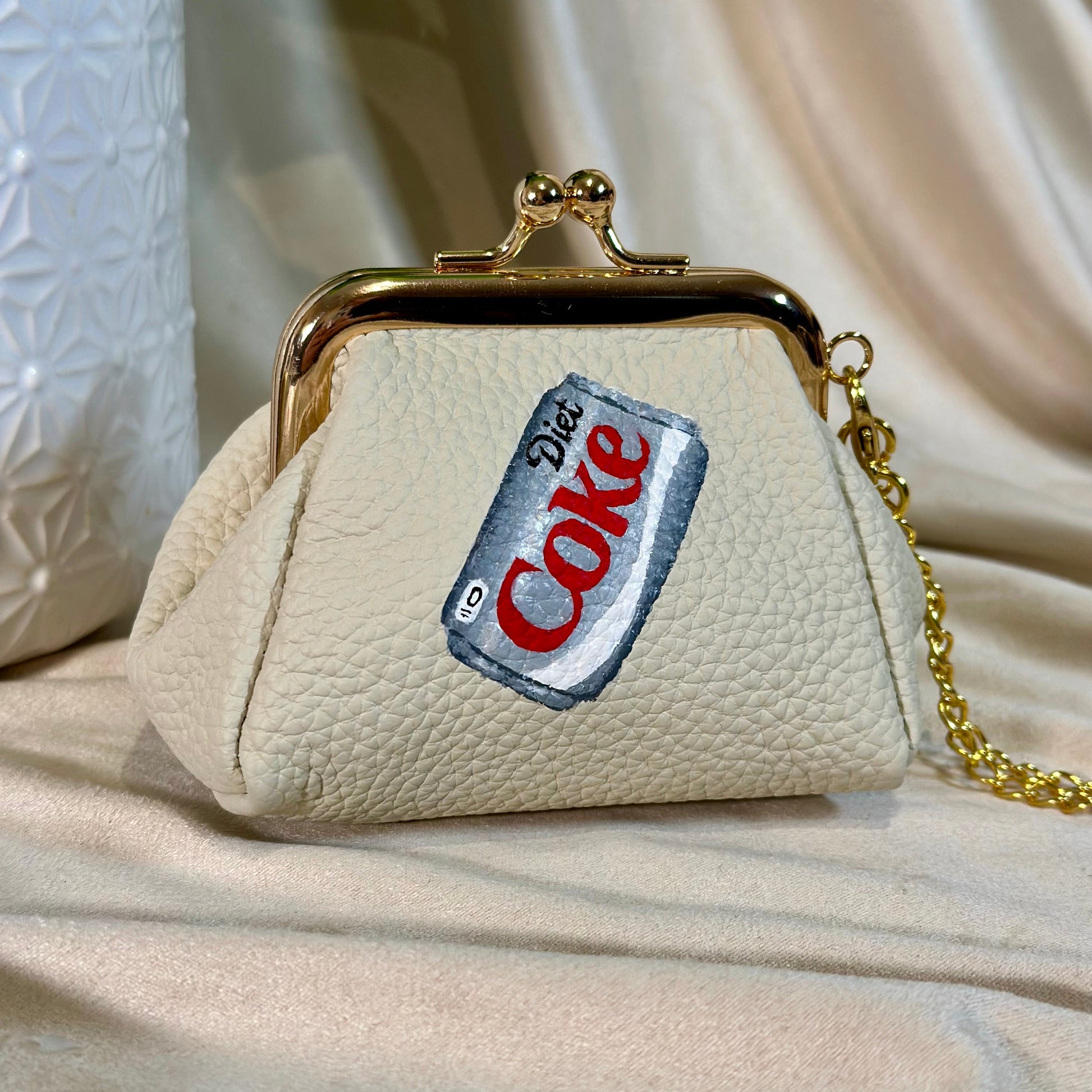 Beige handbag with a Diet Coke label patch on a beige fabric background
