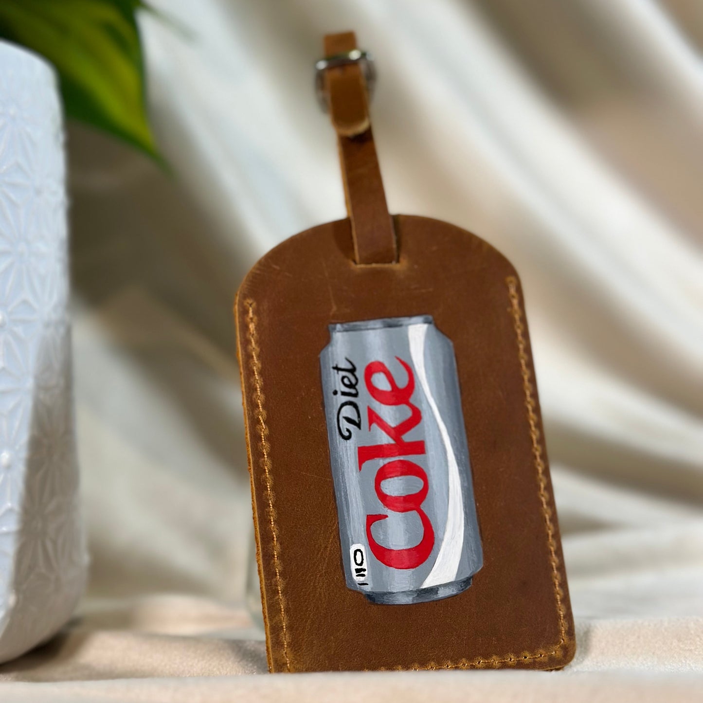 Brown leather luggage tag with Diet Coke can design on a neutral background