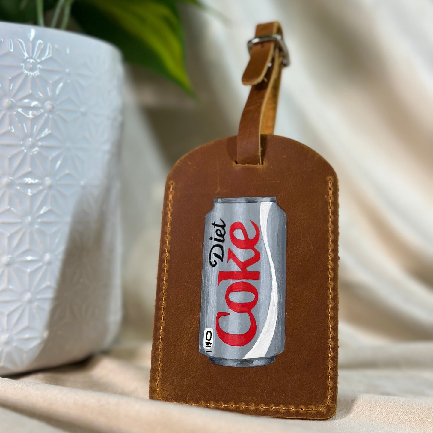 Brown leather luggage tag with Diet Coke can design on a neutral background