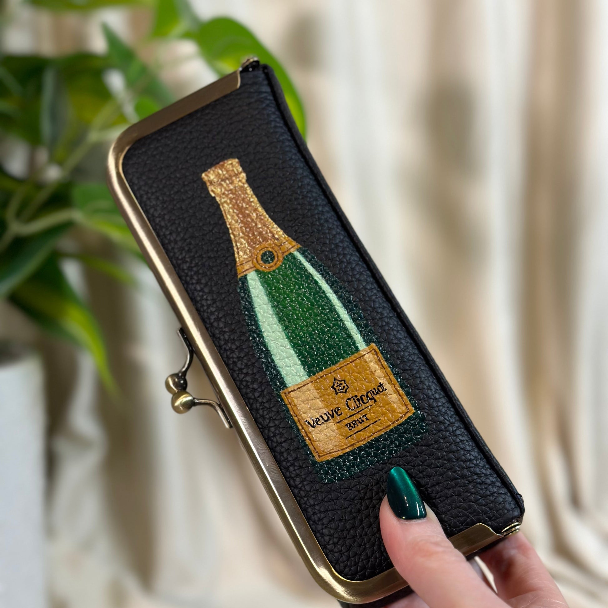 Phone case with champagne bottle design held by a hand against a neutral background