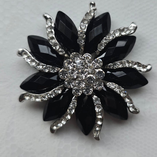 Black flower-shaped brooch with crystal-like stones on a light gray background
