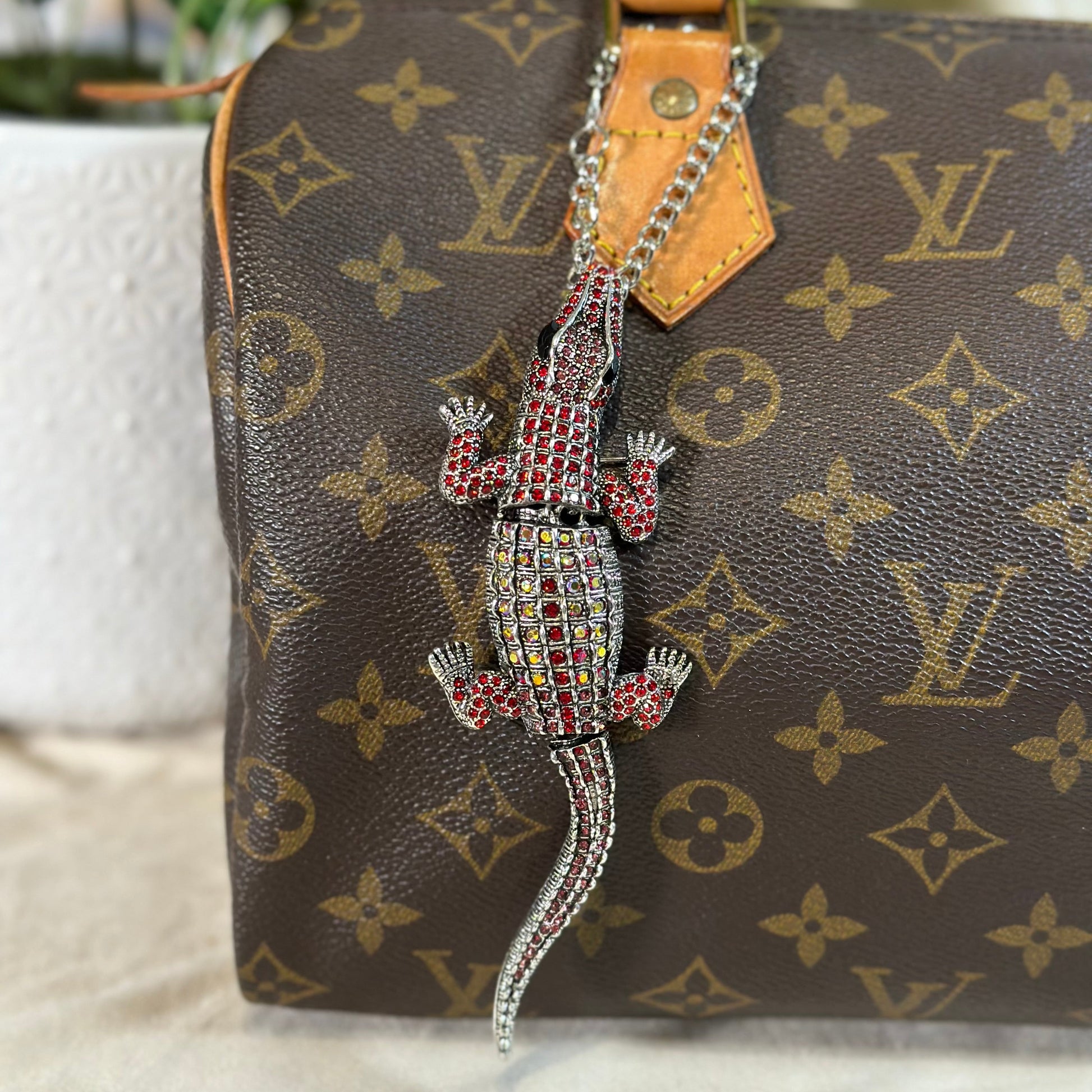 Louis Vuitton handbag with a decorative crocodile charm on a textured surface.