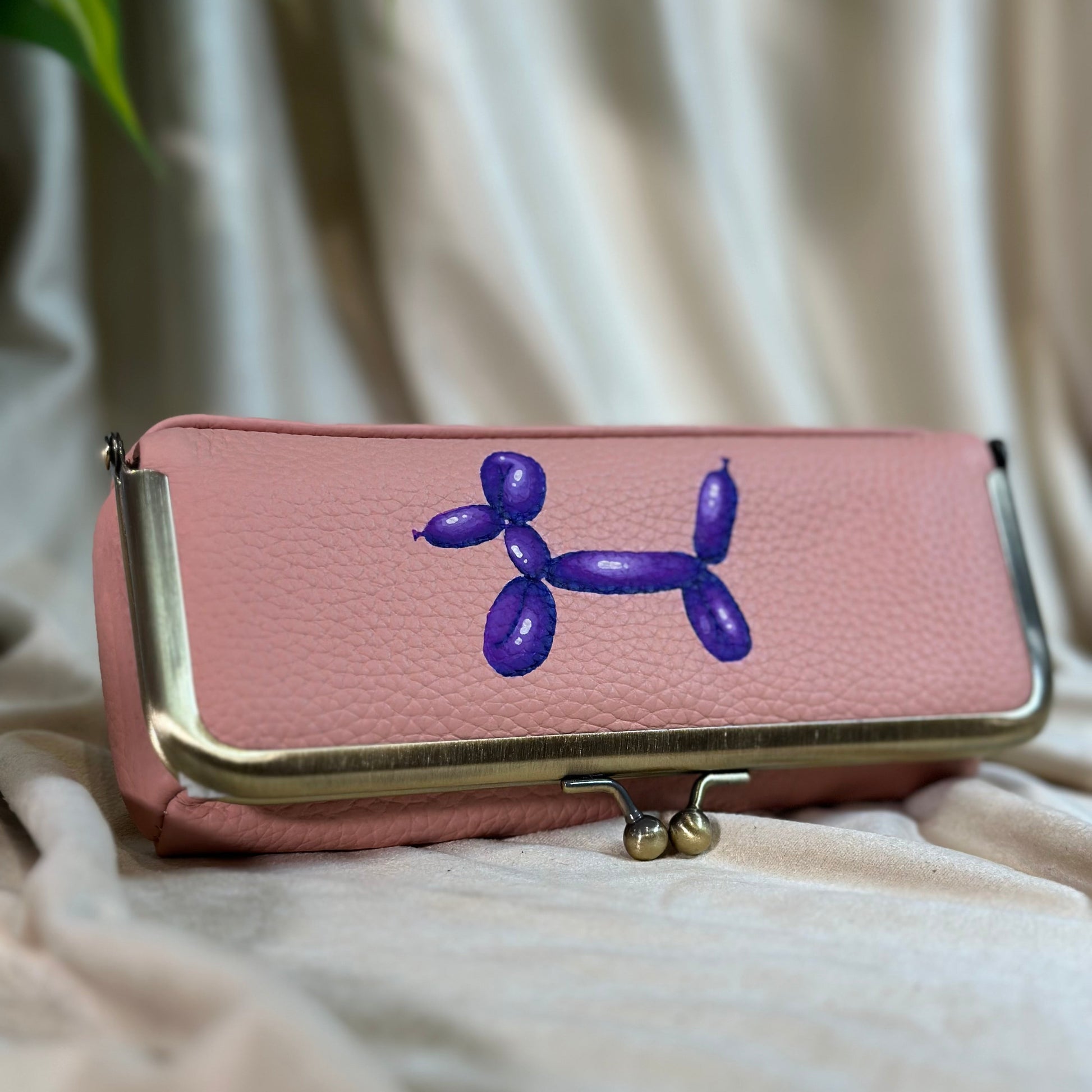 Pink wallet with a blue balloon dog design on a beige surface