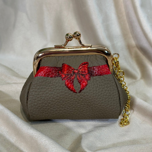 Small clutch purse with gold frame and red bow on a white fabric background