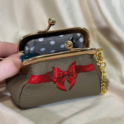 Handbag with red bow design held by a hand against a beige fabric background