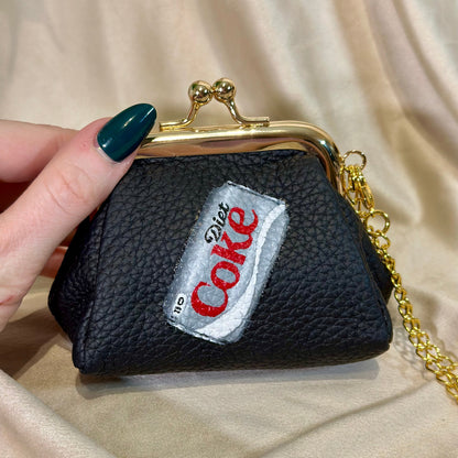 Black pouch with a Coca-Cola patch held by a hand on a beige fabric background