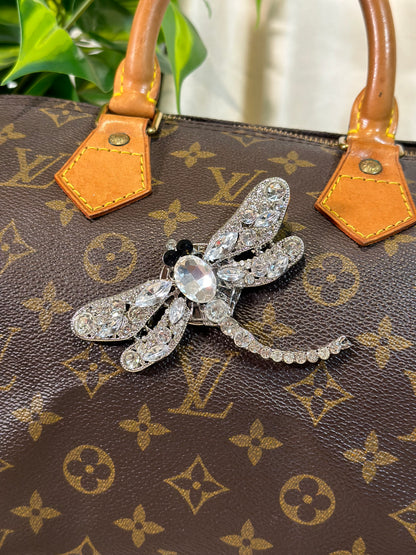 Silver bee-shaped brooch on a Louis Vuitton handbag with monogram pattern.