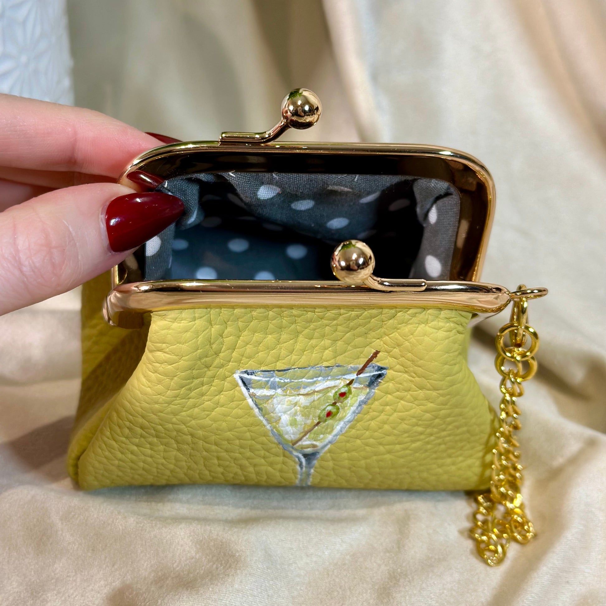 Yellow purse with a martini glass design held by a hand against a neutral background