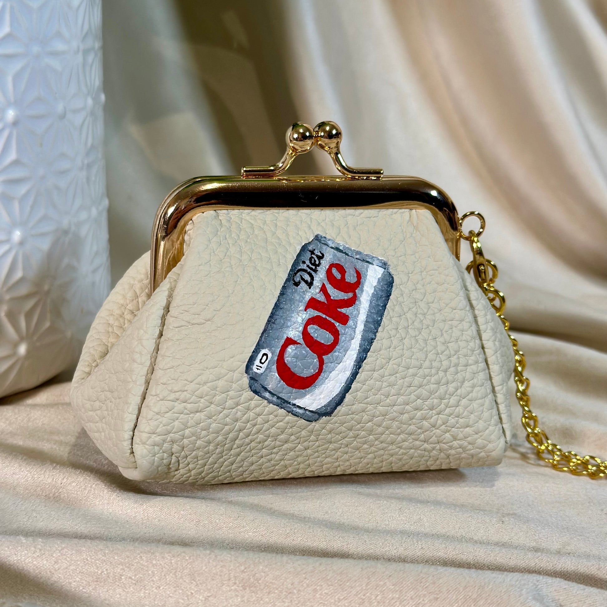 Beige handbag with a Diet Coke label patch on a beige fabric background