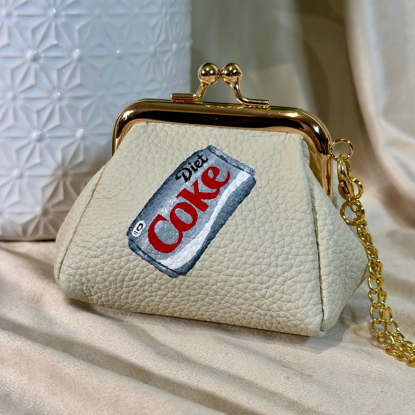Small cream-colored purse with a Diet Coke label design on a beige surface.