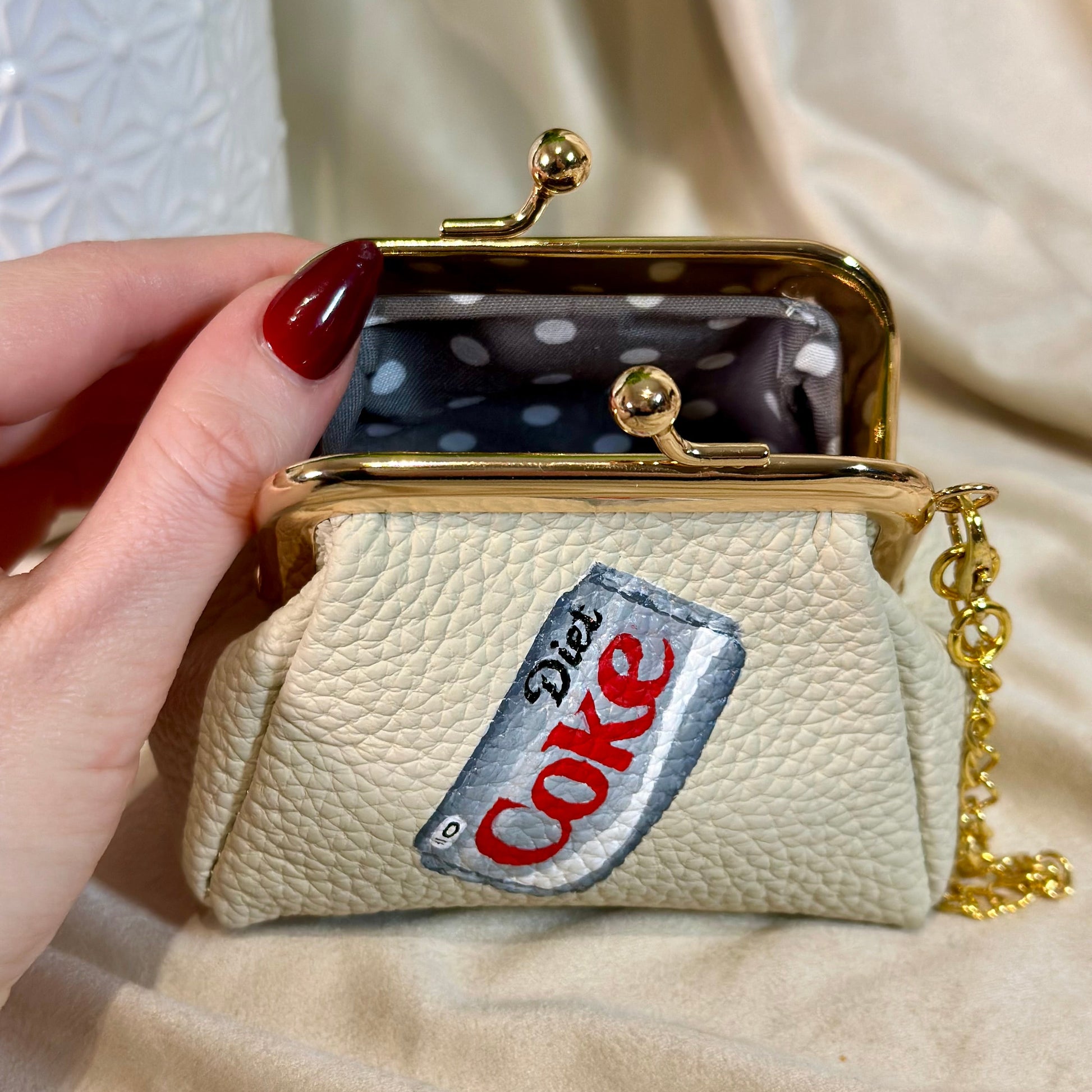 Beige coin purse with Diet Coke logo held by a hand against a neutral background