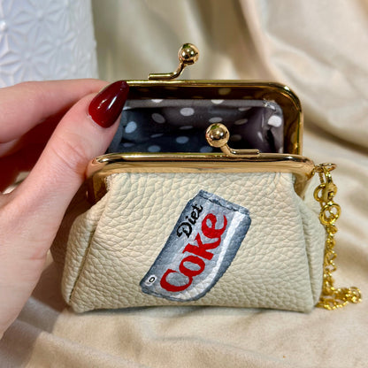 Beige coin purse with Diet Coke logo held by a hand against a neutral background