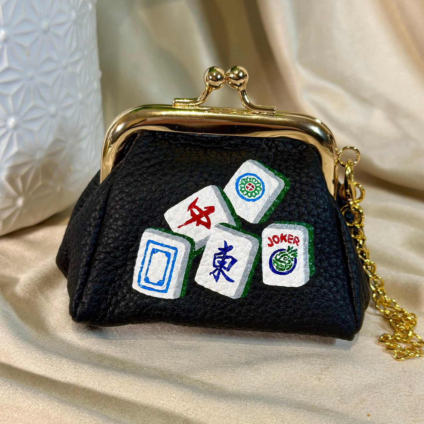 Black purse with Mahjong tile designs on a beige fabric background