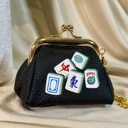 Black purse with Mahjong tile designs on a beige fabric background